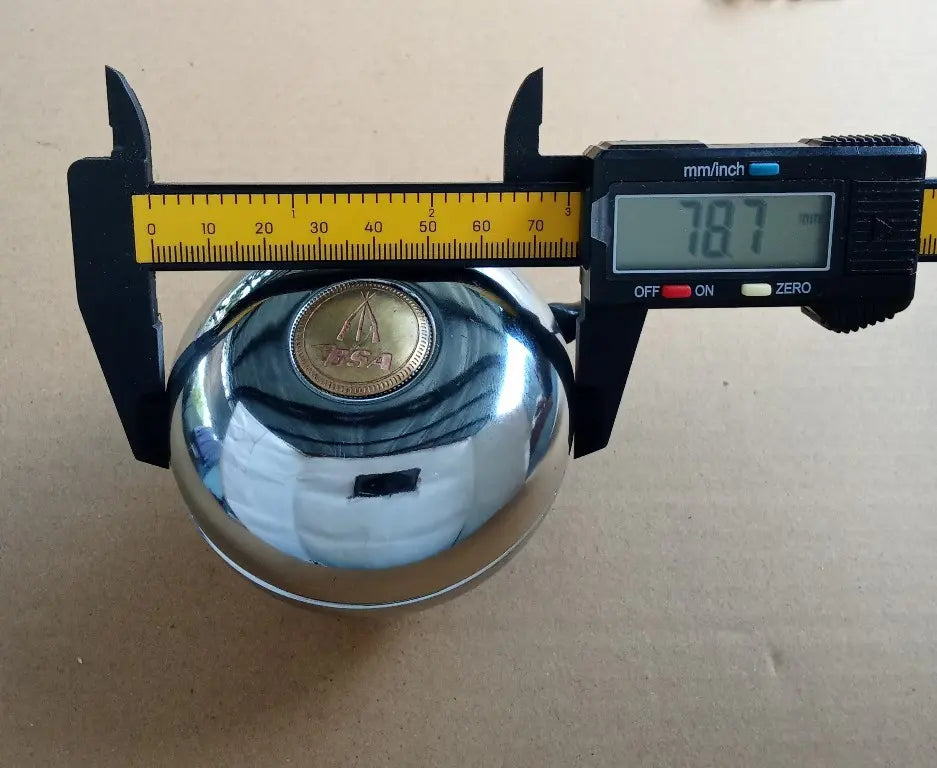 Chrome bell BSA logo with digital caliper measuring its diameter on a beige background