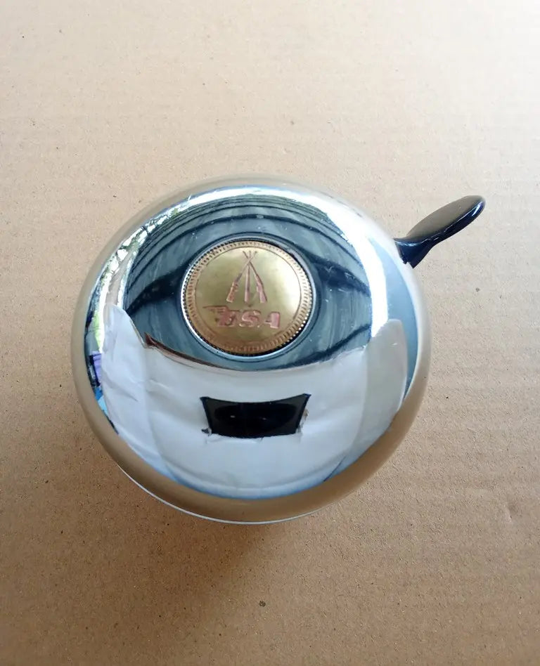 Chrome bell BSA with a BSA gold emblem on a beige background