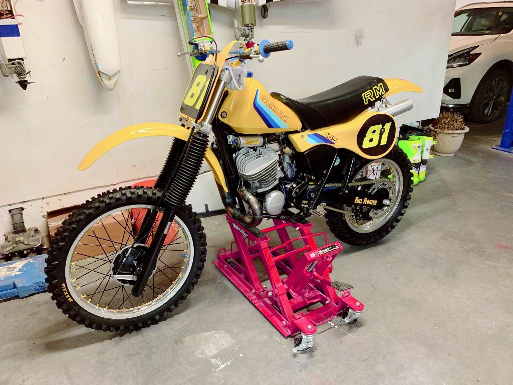 Yellow dirt bike with number 81 on a pink stand in a garage.
