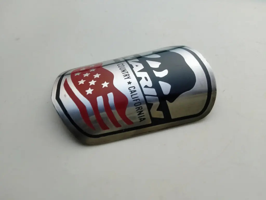 Side profile perspective showing the slim etched stainless steel construction of the Marin emblem.