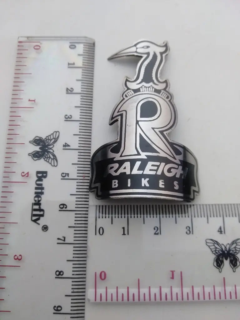 Measurement guide showing height and width dimensions of the handmade Raleigh stainless emblem.